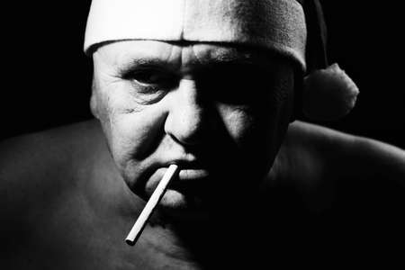 Close up black and white portrait of ominous mature man in Santa Claus hat and with cigarette in his mouthの写真素材