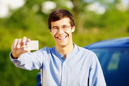 Smiling young man in glasses showing his driving license outdoor in sunny summer dayの写真素材
