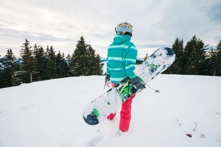 Rear view of snowboarder with snowboard standing on top of ski slope looking on ski trackの写真素材