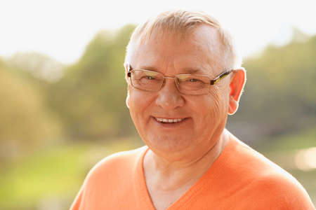 Close up sunny portrait of smiling middle aged man in glasses and orange sweater enjoying fresh airの写真素材