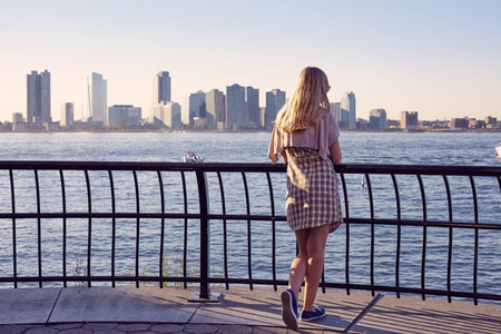 Back view of blonde young woman leaning on berth railing in port on sunny summer dayの写真素材