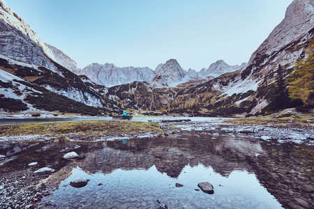 Magnificent landscape with female tourist resting on bench near mountain lakeの写真素材