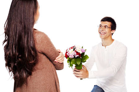 Young smiling man in glasses down on one knee giving bouquet of flowers to young woman on white isolated backgroundの写真素材