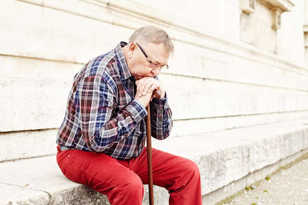 Closeup portrait of pensive mature man in glasses and plaid shirt resting leaning on his wooden walking stickの写真素材