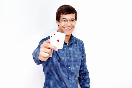 Young hispanic man wearing blue shirt and glasses smiling and holding two aces (clubs and hearts) in...
