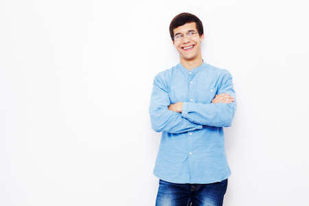 Young hispanic man wearing jeans and glasses standing with crossed arms and smiling against white wallの写真素材