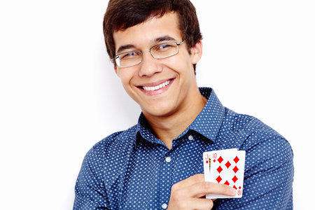 Close up portrait of young hispanic man wearing blue shirt and glasses holding Jack Ten in his hand and smiling against white wall - gambling conceptの写真素材