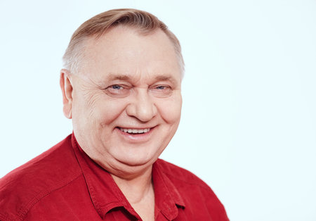 Close up portrait of smiling aged man wearing red shirt against white background - retirement conceptの写真素材