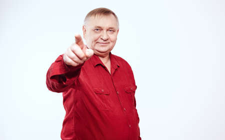 Aged man wearing red shirt standing and pointing at camera with his index finger against white background - choice conceptの写真素材