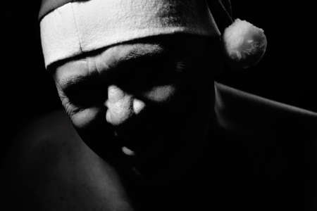 Black and white close up portrait of evil laughing aged man wearing Santa Claus standing against black background - worst Christmas conceptの写真素材