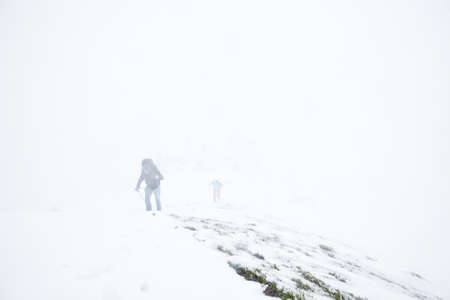 Male and female mountain climbers with huge backpacks and trekking poles having hard hiking trip during winter storm in Austrian Alpsの写真素材
