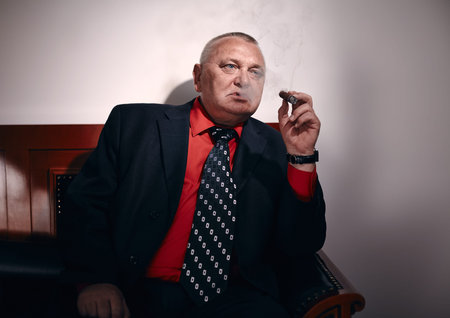 Serious middle aged businessman wearing black suit, red shirt and wristwatch sitting on old...