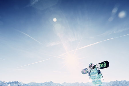 Female snowboarder wearing colorful helmet, blue jacket and grey gloves standing with snowboard in...