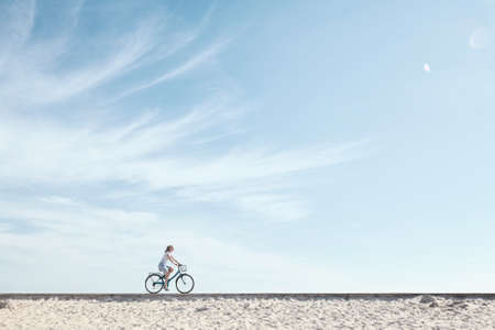 Young woman riding bicycle with basket against blue sky during summer - healthy lifestyle conceptの写真素材