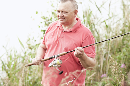 Portrait of smiling middle aged man wearing polo shirt, angling with rod and spinning reel on summer...