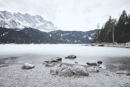Young female hiker with backpack enjoying view to frozen lake Eibsee, winter Bavarian forest and...