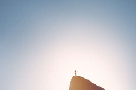 Silhouette of happy woman wearing skirt standing with outstretched arms on top of hill and celebrating achievement over sky and sun light on sunrise or sunset - inspiration concept with copy spaceの写真素材