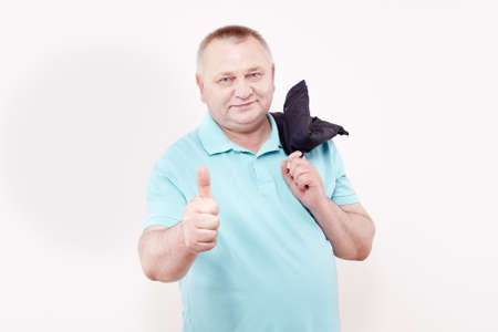 Cheerful middle aged man wearing blue shirt, holding jacket over his shoulder and showing thumb up hand gesture against white wall - success conceptの写真素材