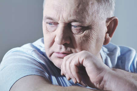 Close up portrait of thoughtful aged man in t-shirt sitting with hand on chin - depression conceptの写真素材
