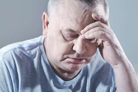 Close up portrait of thoughtful aged man in t-shirt sitting with hand on head - depression conceptの写真素材