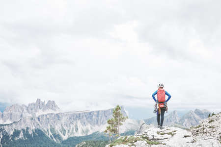 Female mountaineer with backpack, helmet and harness with climbing gear enjoying stunning view to...