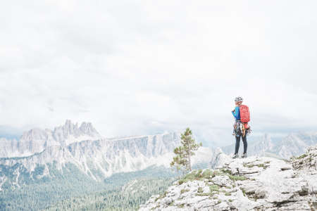Female mountaineer with backpack, helmet and harness with climbing gear enjoying stunning view to mountains during summer day in Dolomite Alps - mountaineering, sport climbing or adventure conceptの写真素材