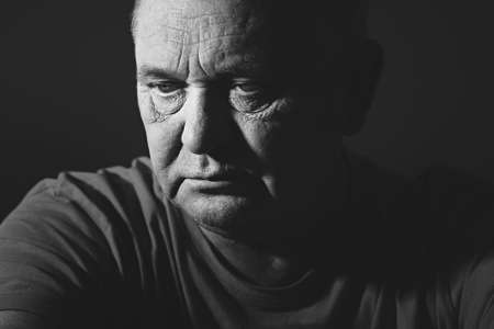 Close up portrait of aged man wearing t-shirt against black background - depression conceptの写真素材