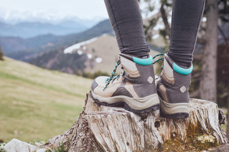 Close up of female classic leather hiking boots wearing by woman standing on stump in mountains -...