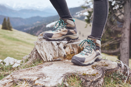 Close up of female classic leather hiking boots wearing by woman standing on stump in mountains - travel and outdoor activities conceptの写真素材