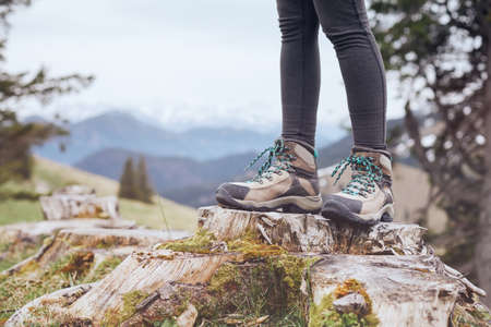 Close up of female classic leather hiking boots wearing by woman standing on stump in mountains -...
