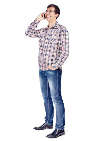 Full body half turn view portrait of smiling young man talking on mobile phone wearing metal frame glasses, checkered shirt, blue jeans and black shoes isolated on white backgroundの写真素材