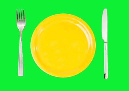 Yellow dish with a knife and fork on green backgroundの写真素材