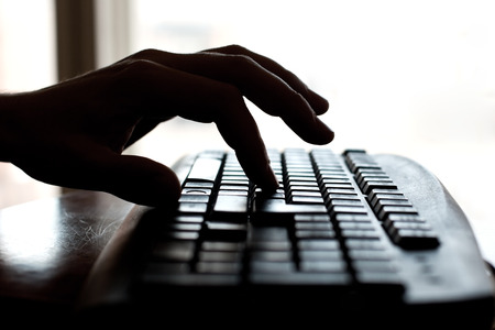 Silhouette of a hand on a computer keyboardの写真素材