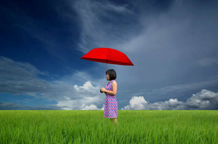 young woman with red umbrella in a green field under rainの写真素材