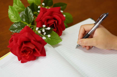 hand holding pen writing on notebook with roseの写真素材