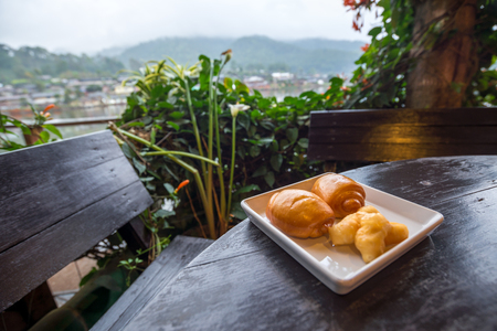 Fried steamed buns in white plate on the wooden table with river and mountain view behind garden, Traveling in Thailandの写真素材