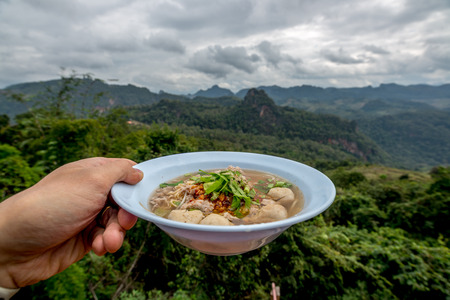 Tom Yum Noodle in hand with mountain view in behind, Thai signature food with naturalの写真素材