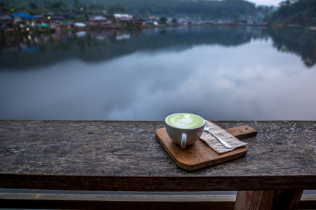 Hot Matcha Latte in white cup on the wood porch with village river view, Countryside of Thailandの写真素材