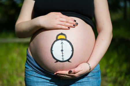 Pregnant woman with clock painted on her bellyの写真素材