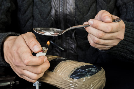 The use of illegal drugs, drugs. A man preparing heroin, using a spoon and a lighter. Illegal drugs.の写真素材