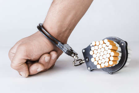 Cigarettes and hand of a man in handcuffs. The concept of nicotine addiction, a bad habit. Isolated on a white background.の写真素材