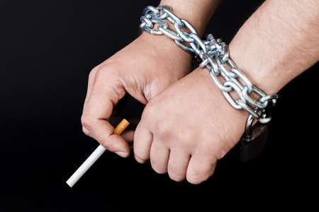 Cigarettes and hand of a man tangled in chains . The concept of nicotine addiction. Isolated on black background.の写真素材