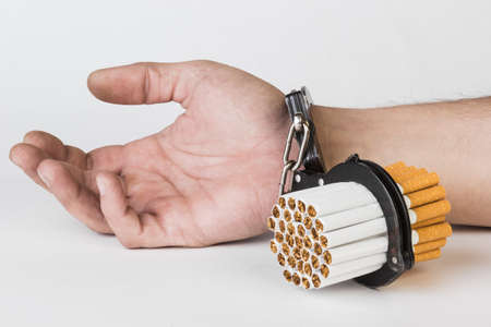 Cigarettes and hand of a man in handcuffs. The concept of nicotine addiction, a bad habit. Isolated on a white background.の写真素材