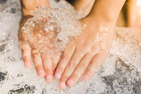 Hands of a boy with a splash of water, backlit in the evening sun.の写真素材