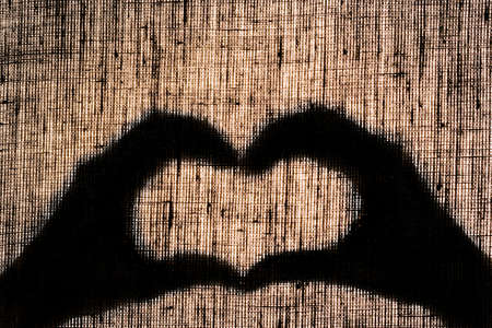 Shadow hands and fingers in the shape of a heart on linen canvas.の写真素材