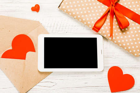 Digital tablet with gifts and hearts on a wooden table. View from above. Valentines Day concept. on white wooden background.の写真素材