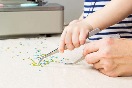 Mother and child make a pattern of beads on the fabric. Workplace for handicraft creativity.の写真素材