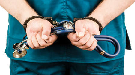 Close-up Of Doctor Hands With Stethoscope In Handcuffs. The concept of medicine and crime.の写真素材