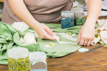 A woman is making jewelry, a home workshop. Female hands that create an accessory with beads and ribbons. Beauty, creativity, the concept of handicraftの写真素材