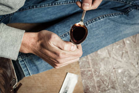 The hands of a drug addict melting cocaine in a spoon. A man holds a spoon over a cigarette lighter. Drugs and the concept of crime.の写真素材